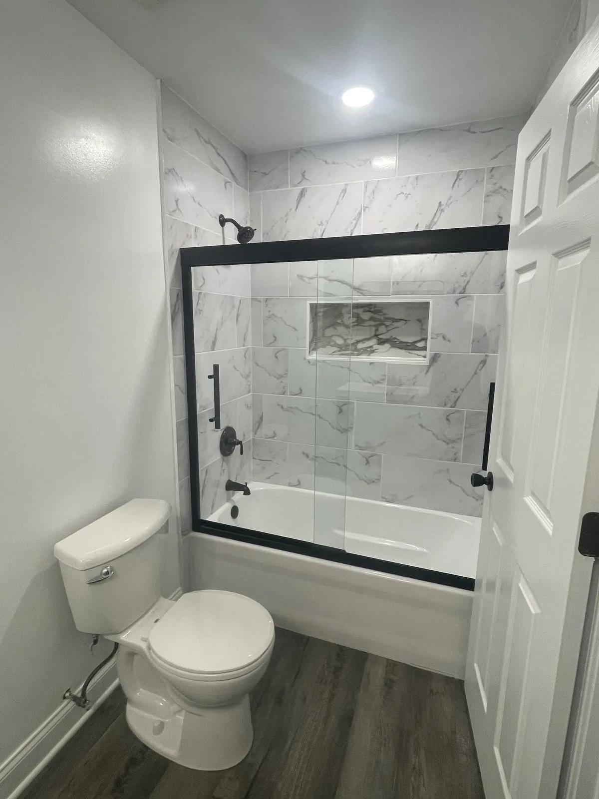 New marble-tiled Aurora tub and shower with black-framed glass after remodeling